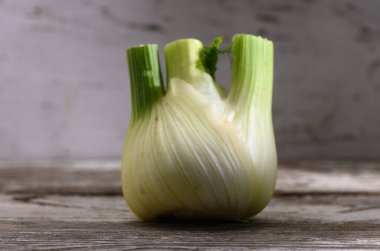 A vibrant fennel bulb with green stalks stands proudly on a weathered wooden table, illuminated by soft afternoon light. clipart