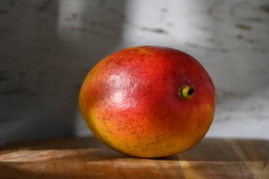 Olgun bir mango, yumuşak güneş ışığıyla aydınlatılan ılık bir ahşap zemin üzerinde dinlenirken zengin renklerini sergiler..