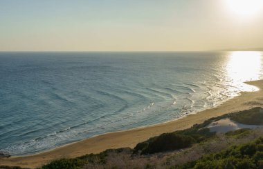 Güneş yavaşça batar, sakin okyanus dalgaları üzerine sıcak bir parıltı yayar, aşağıdaki kumlu kumsalı öperken.