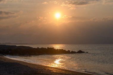Güneş sakin suların üzerinde batarken sıcak renkler gökyüzünde karışıyor ve kıyı şeridinde sakin bir atmosfer yaratıyor..