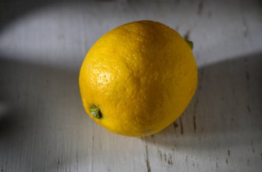 Altın limon, aşınmış ahşap üzerinde zarif bir şekilde duruyor. Canlı rengini ve engebeli dokusunu hafif güneş ışığında sergiliyor..