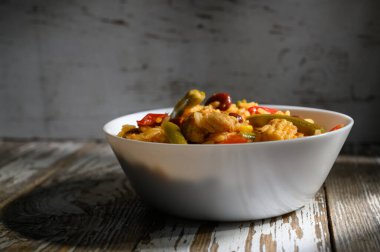 Lezzetli ve canlı sebzelerle dolu pirinçler beyaz bir kasede dinleniyor. Masanın kırsal cazibesini vurguluyor..