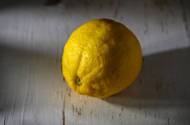 Canlı bir limon, yıpranmış bir masada tek başına oturur. Yumuşak güneş ışığıyla aydınlatılır ve dokusunu ön plana çıkarır..