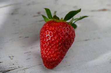 Canlı kırmızı bir çilek, yumuşak güneş ışığıyla aydınlatılan, sulu dokusunu gözler önüne seren, kırsal ahşap bir yüzeye dayanır..