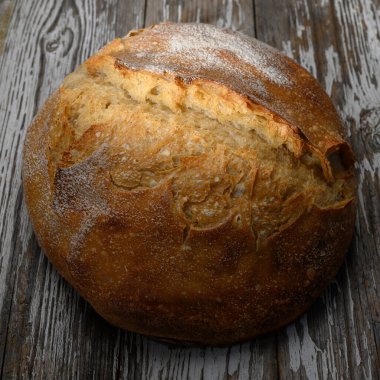 A warm round loaf of bread sits on a wooden table, showcasing its golden crust and artisanal texture. clipart