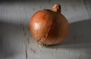 Kahverengi bir soğan yıpranmış ahşap bir yüzeyde oturur. Yüzeyi yumuşak doğal ışığı yansıtır ve çatlaklarını aydınlatır..