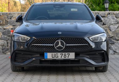 Gaziveren Kıbrıs Rum Kesimi -03.02.2025 Şık siyah sedan, berrak gökyüzünün altında kırsal taştan bir duvarın önünde modern tasarımı sergiliyor.