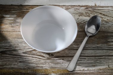 Yumuşak ışık filtreleri temiz, boş bir kase ve eski ahşap bir yüzey üzerinde metalik kaşık üzerinde, basitliği çağrıştırıyor..