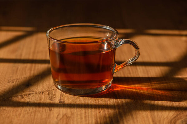 Golden afternoon sunlight casts shadows on a glass of tea, enriching its deep amber color on a wooden table.