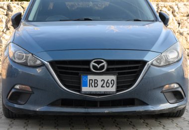 Gaziveren Kıbrıs Rum Kesimi -03.02.2025 Modern mavi renkli kompakt bir araba sıcak güneş ışığı altında dokulu taş bir duvara park etmiş, tasarımını vurguluyor.