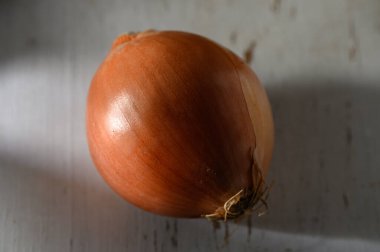 Güneş ışığı, taşralı ahşap bir masada dolgun bir soğan üzerinde parlar, zengin, toprak tonlarını vurgular..