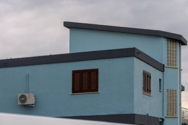 Çarpıcı mavi bir bina kasvetli bir gökyüzüne karşı duruyor, modern çizgilerini ve eşsiz mimari özelliklerini sergiliyor..