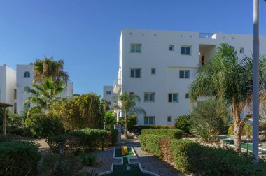 Bereketli yeşillik ve yollarla dolu sakin bir bahçe, parlak beyaz konut binalarının arasına kurulmuş..