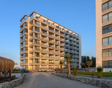 Gün batımında, bereketli yeşilliklerin ve kıyı şeridindeki palmiye ağaçlarının arasına kurulmuş gösterişli bir konutun üzerine ılık bir ışıltı yayılıyor..