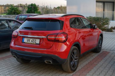 Gaziveren Kıbrıs Rum Kesimi - 30.01.2025 Zarif bir kırmızı SUV şık bir tatil köyünün önüne park edilmiş, yumuşak akşam ışığı altında modern tasarımı sergilenmektedir..