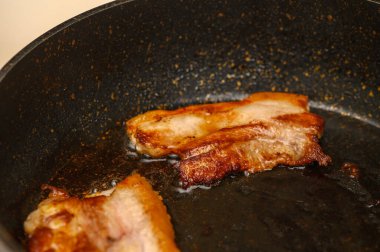 Sulu domuz pastırması şeritleri siyah bir tavada yavaşça kızarır ve mutfağı dolduran lezzetli bir koku yayar..