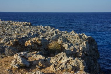 Dalgalar engebeli kayalara çarpar, güneş batarken, sakin denize altın renkler serer..