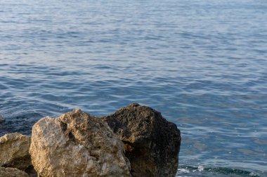Sakin kıyı şeridinde sabah ışığında sakin, kristal berrak sulara zıt engebeli kayalar yer alıyor..