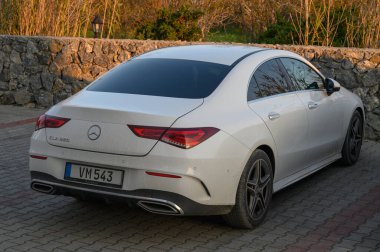 Gaziveren Kıbrıs Rum Kesimi -30.01.2025 entellektüel beyaz bir araba, alacakaranlığın ılık parıltısıyla aydınlanan taştan bir bariyerin yanında duruyor..