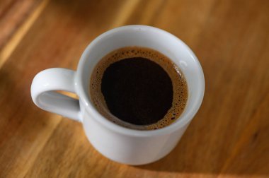 Derin kahverengi sıvı, sıcak ahşap bir yüzey üzerinde duran küçük beyaz bir fincanda davetkar bir şekilde kıvrılır, tadını çıkarmak için mükemmeldir..