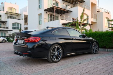 Gaziveren Cyprus -30.01.2025 A stylish black coupe rests quietly in front of a contemporary building, bathed in warm evening sunlight. clipart