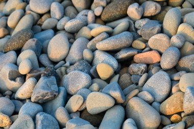 Pürüzsüz, renkli çakıl taşları güzel bir günbatımında sakin kıyı şeridi boyunca uzanır, kumların üzerine yumuşak gölgeler bırakır..
