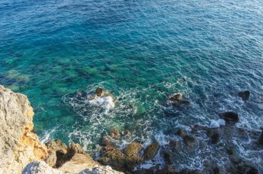 Dalgalar yavaşça kayaların üzerinde yuvarlanarak canlı mavi okyanus sularının yanında dingin bir atmosfer oluşturur..