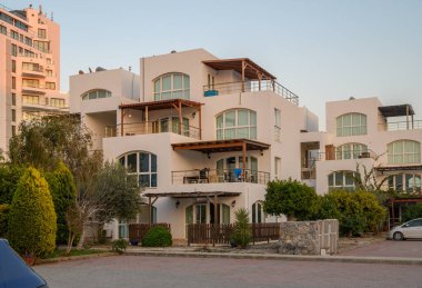 Büyüleyici, modern bir bina. Geniş pencereleri güneş batarken, yemyeşil bahçeler ve ağaçlarla çevrili..