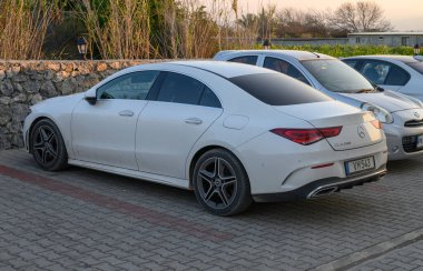 Gaziveren Kıbrıs Rum Kesimi - 30.01.2025 Modern beyaz bir sedan alacakaranlık sırasında yemyeşil bitki örtüsüyle çevrili sakin bir park alanında dinleniyor.