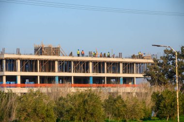 Bir grup inşaat işçisi bir inşaat sahasında, sakin bir ağaç zeminine karşı bir yapı oluşturmakla meşgul..