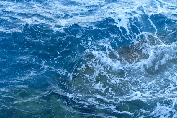 Turkuaz su, su altındaki kayaların üzerinde enerjik bir şekilde döner ve güneşin altında çarpıcı bir su dansı yaratır..