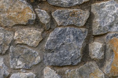Değişik kaya boyutları ve toprak renkleri olan taştan bir duvarın yakın çekimi, zamansız işçilik sergiliyor..