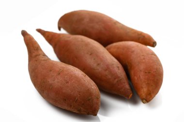 Dört tatlı patates temiz beyaz bir zeminde dinleniyor, ayırt edici formlarını ve zengin renklerini sergiliyorlar..