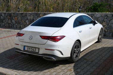 Gaziveren Kıbrıs Rum Kesimi -15.02.2025 Modern sedan güneş ışığında parıldıyor, engebeli taş bir duvarın yanında park halindeyken zarif tasarımını sergiliyor.