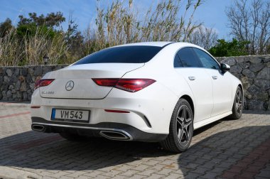 Gaziveren Kıbrıs Rum Kesimi -15.02.2025 Şık bir sedan güneşte güneşleniyor, yeşillik ve desenli taşla çerçevelenmiş, dingin bir hava yaratıyor.