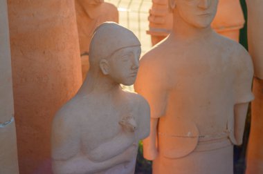 Sculptures in warm terracotta tones capture the essence of human figures, surrounded by natural light outdoors. clipart