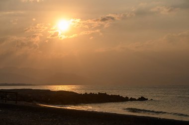 Siluetli bulutlar güneş ışığını yansıtıyor, sakin bir atmosfer yaratıyor huzur dolu sahil boyunca, alacakaranlıkta..