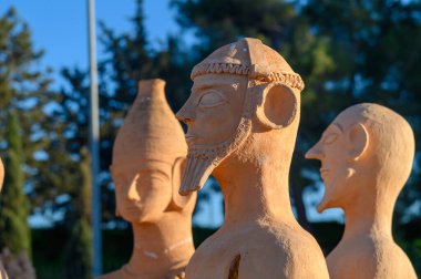 Terracotta heykelleri antik figürleri andırıyor sakin bir bahçede duruyor, parlak bir gökyüzünün altında güneşleniyorlar..