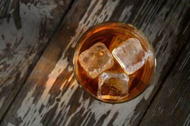 Soğuk bir içecek ve buzla dolu bir bardak yıpranmış ahşap bir yüzeye oturur, sıcaklık ve konfor yayar..