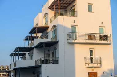 Bir sahil inzivası öğleden sonra canlı mavi gökyüzünün altında zarif balkonlar ve beyaz duvarlar barındırır..