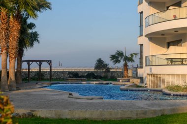 Güneşli bir öğleden sonra, dingin palmiyeler ve zarif mimari ile çevrili sakin bir havuzun yanında gevşeme başlar..