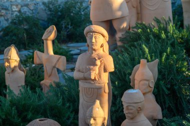 Çeşit çeşit antik figürlerin terakotta heykelleri yemyeşil çimenlikten ortaya çıkarak günbatımının sıcak, parlayan ışığında güneşlenirler..