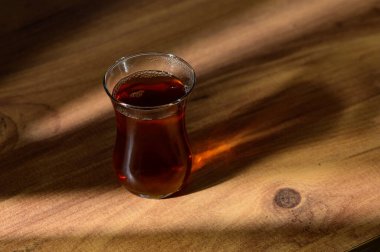 Zengin çayla dolu narin bir bardak, sıcak öğleden sonra ışığını yakalar, koyu rengini ve davetkar aromasını sergiler..