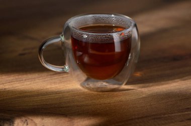 Parlak ahşap üzerinde, güneş ışığı altında aromatik çaylarla dolu cam bir bardak..