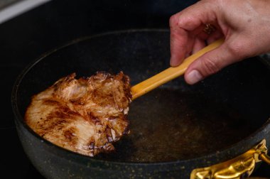 Bir el ustalıkla altın sarısı bir domuz pirzolasını sıcak bir tavada çevirir ve mutfağa lezzetli kokular yayar..