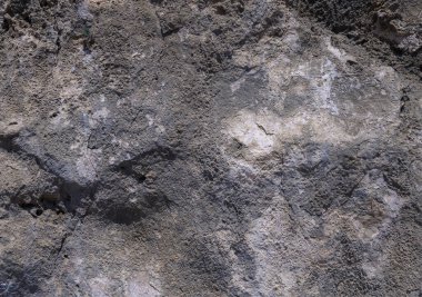 Güneş ışığı, eski bir kaya oluşumunun pürüzlü yüzeyini aydınlatır. Karmaşık dokuları ve jeolojik katmanları ortaya çıkarır..