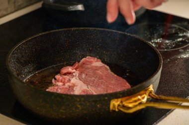 Yumuşak bir parça biftek bir tavada pişiyor, sıcak bir mutfak ortamında lezzetli buhar yayıyor..