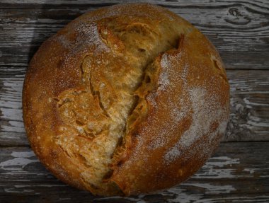 Altından kahverengi bir dış görünüşü olan kabuklu ekmek somunu eski ahşap yüzeyde oturur ve enfes bir aroma yayar..