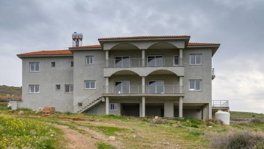 Kemerleri ve balkonları olan, kasvetli bir gökyüzünün altında yeşil tarlalarla çevrili geniş bir villa, köylü cazibesini sergiliyor..