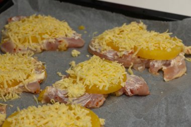 Ananas dilimleriyle katmanlanmış tavuk parçaları ve bol miktarda dilimlenmiş peynir pişirme sürecini bekliyor..